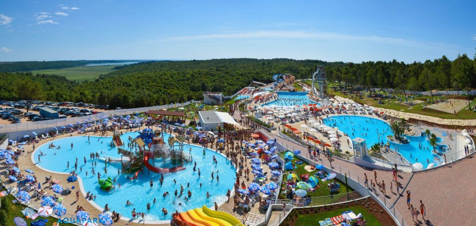 A large outdoor swimming pool area with multiple pools, water slides, and sun loungers.
