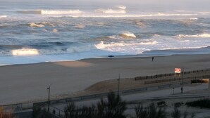 A beach with waves, a person walking, and a sign.