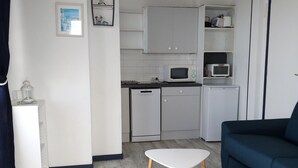 A compact living space with a kitchenette, two white tables, a blue sofa, and a white cabinet.
