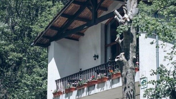Ein weißes Gebäude mit einem hölzernen Balkon, umgeben von üppiger Vegetation.