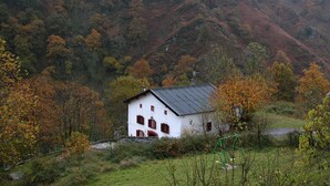 Ein weißes Gebäude mit roten Fensterläden, umgeben von Herbstlaub und einer Bergkulisse.