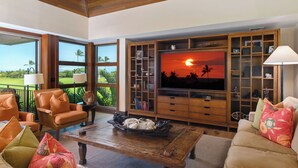 A living room with a television, wooden furniture, and a view of the sunset. - Fairway Villa 120A: Charming w/Shared Pool, AC, 2 Golf Carts & Lanai Ocean Views (Kailua Kona)