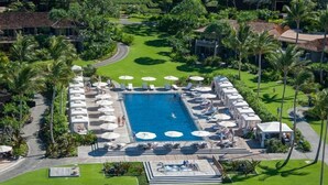 An aerial view of a resort with a central swimming pool, surrounded by lounge areas with umbrellas and sun loungers. - Fairway Villa 120A: Charming w/Shared Pool, AC, 2 Golf Carts & Lanai Ocean Views (Kailua Kona)