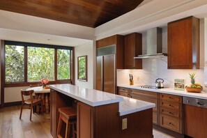A modern kitchen with wooden cabinets, a marble countertop, and a large window with a view of greenery.