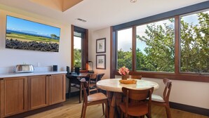 A kitchen with wooden cabinets, a dining table with chairs, a toaster, and a large window with a view of greenery. - Fairway Villa 120A: Charming w/Shared Pool, AC, 2 Golf Carts & Lanai Ocean Views (Kailua Kona)