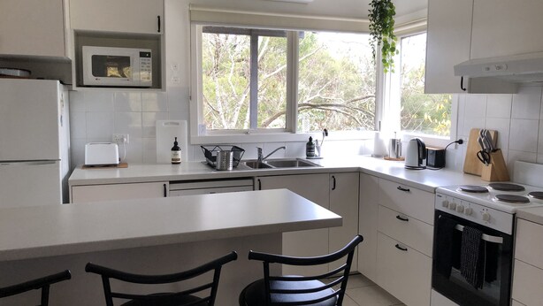 A modern kitchen with white cabinets, a built-in microwave, a sink, and a stove. There are two black chairs at the kitchen island. - Bird Hill - A Garden Retreat in the Yarra Valley - Get Up Close to Native Birds (Woori Yallock)