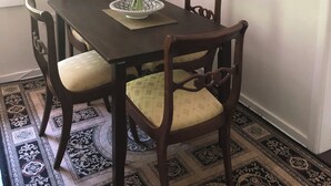 A dining area with a dark wooden table, four chairs, a vase of flowers, and three framed pictures on the wall. - Bird Hill - A Garden Retreat in the Yarra Valley - Get Up Close to Native Birds (Woori Yallock)