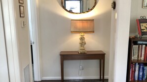 A hallway with a patterned rug, a table with a lamp, a mirror, and a bookshelf with books and games. - Bird Hill - A Garden Retreat in the Yarra Valley - Get Up Close to Native Birds (Woori Yallock)
