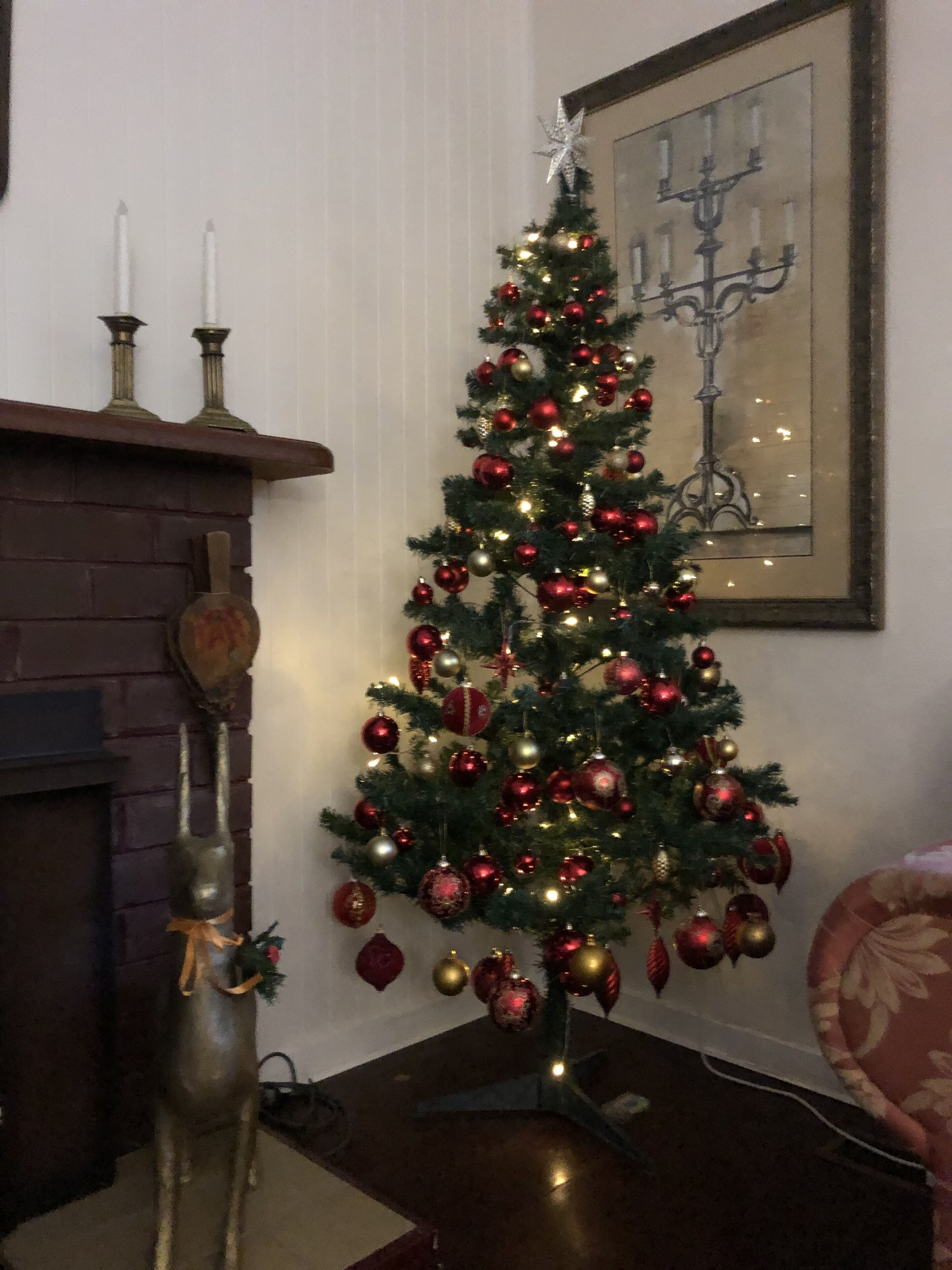 A decorated Christmas tree with ornaments and lights, a candelabra, and a framed artwork on the wall.