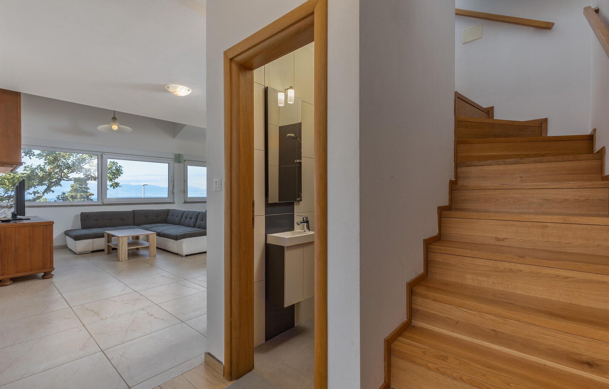 Un intérieur moderne avec un escalier en bois, un coin salon comprenant un canapé et une table, et une cuisine équipée d’un évier et de placards.
