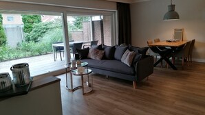 A modern living room with a dark grey sofa, a glass coffee table, and a dining area with a wooden table and chairs. - Apartment with hotel comfort (Bad Rothenfelde)