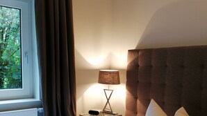 A hotel room with a bed, a nightstand, a lamp, and a window with curtains. - Apartment with hotel comfort (Bad Rothenfelde)