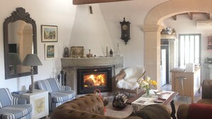 Una sala de estar acogedora con chimenea, sofás a rayas, un sillón de cuero marrón y un comedor con una mesa lista para dos.
