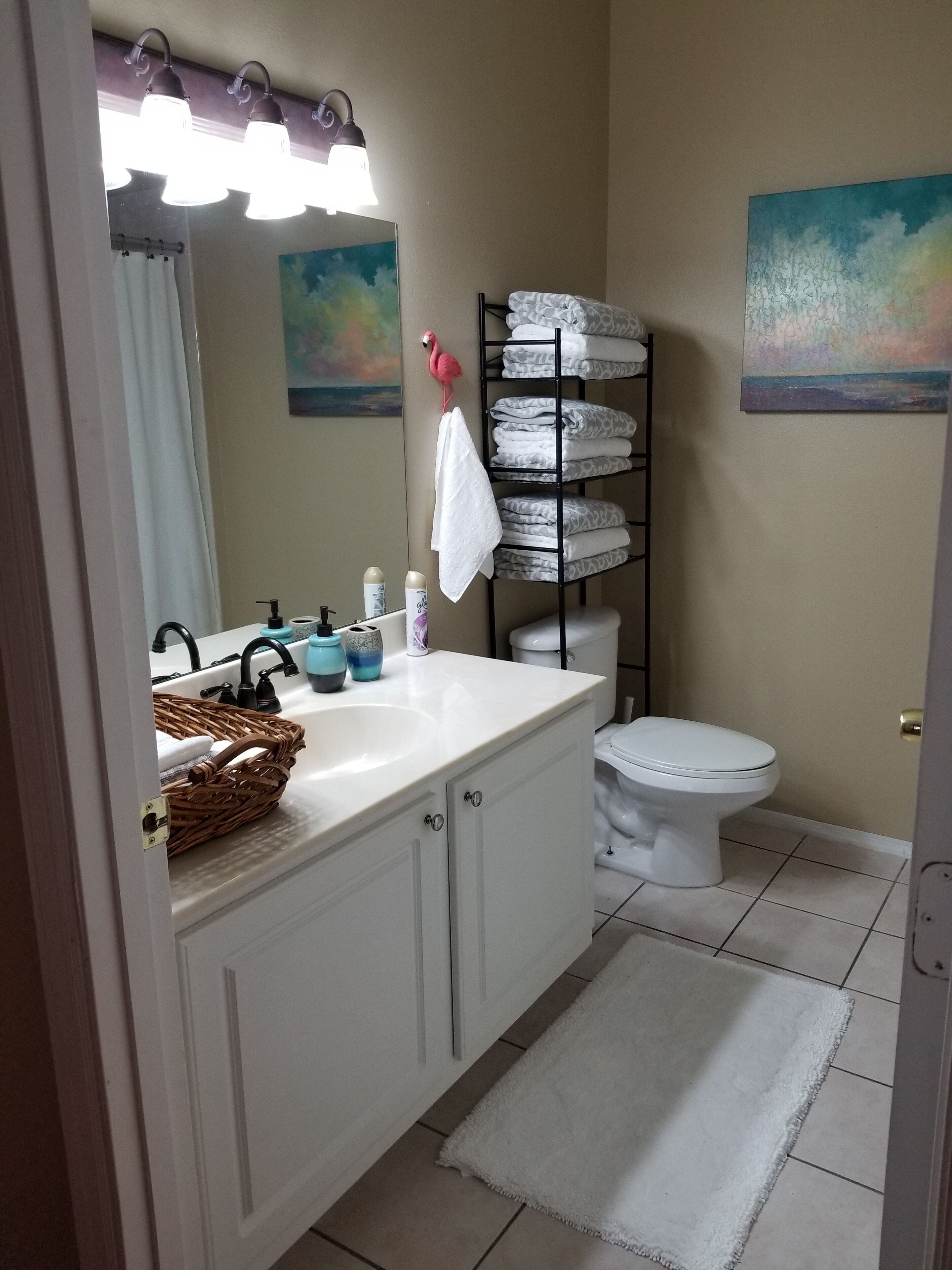 A bathroom with a white vanity, a toilet, a towel rack, and a shelf with folded towels.