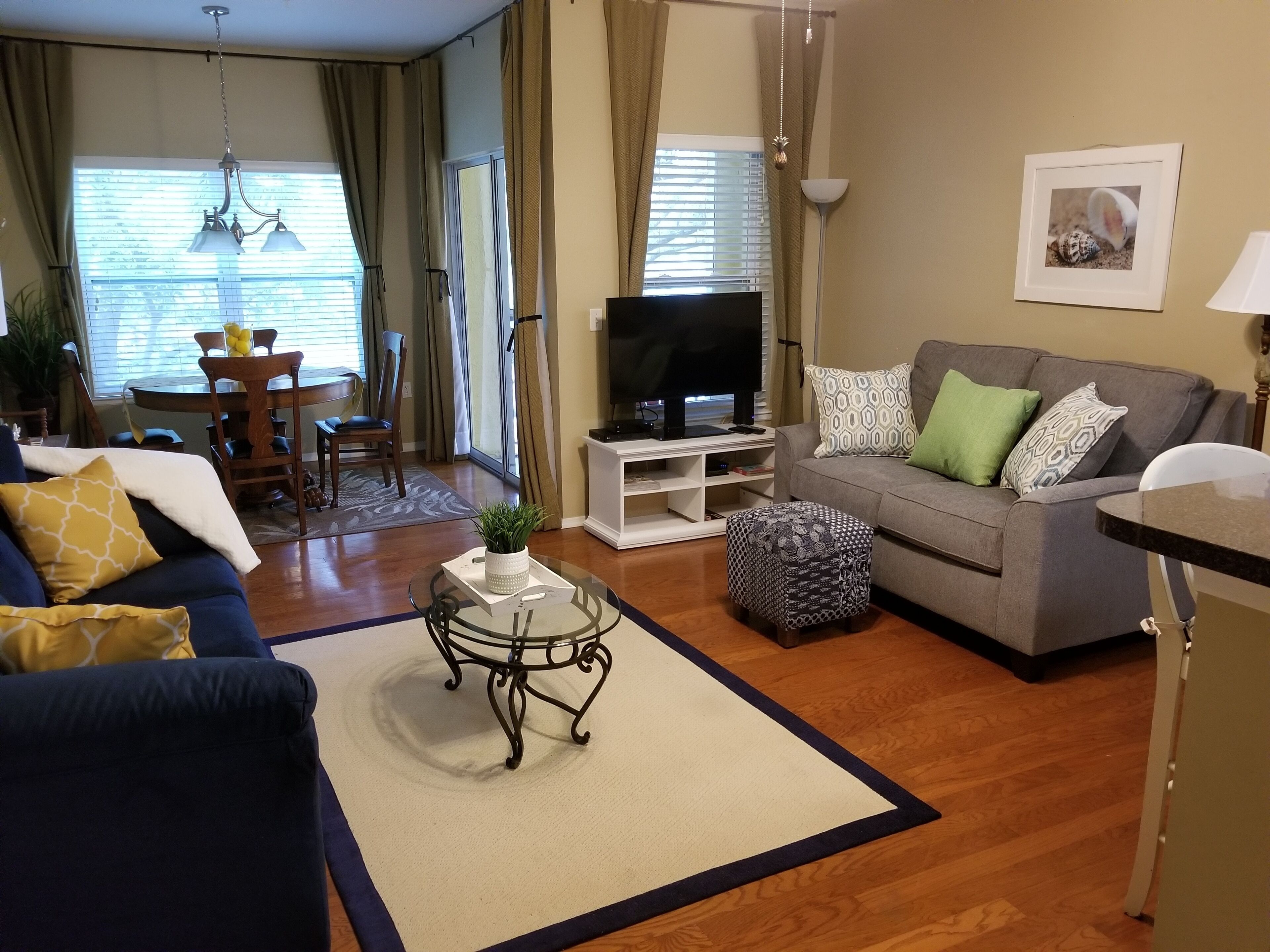 A living room with a sofa, ottoman, coffee table, TV, and dining area with chairs and a table.