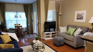 A living room with a sofa, ottoman, coffee table, TV, and dining area with chairs and a table. - 5 min. to Madiera Beach, Fl. GATED. PERFECT & COZY! (Seminole)