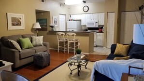 A living room with a sofa, chairs, a coffee table, and a kitchen area with cabinets and appliances. - 5 min. to Madiera Beach, Fl. GATED. PERFECT & COZY! (Seminole)