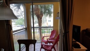 A room with a table, chairs, a TV, and a balcony with a palm tree and red chairs. - 5 min. to Madiera Beach, Fl. GATED. PERFECT & COZY! (Seminole)