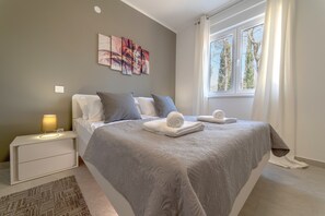 A bedroom with a bed, nightstand, lamp, artwork, and a window with curtains.