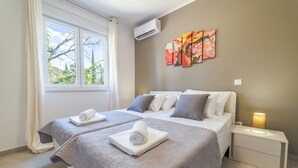 Une chambre d’hôtel avec deux lits, une fenêtre avec des rideaux, un climatiseur, une table de chevet avec une lampe et un tableau au mur.