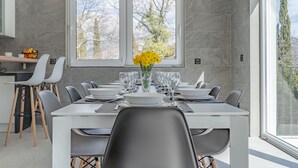 Un espace de salle à manger moderne avec une longue table dressée pour six personnes, des chaises blanches et un vase rempli de fleurs jaunes.