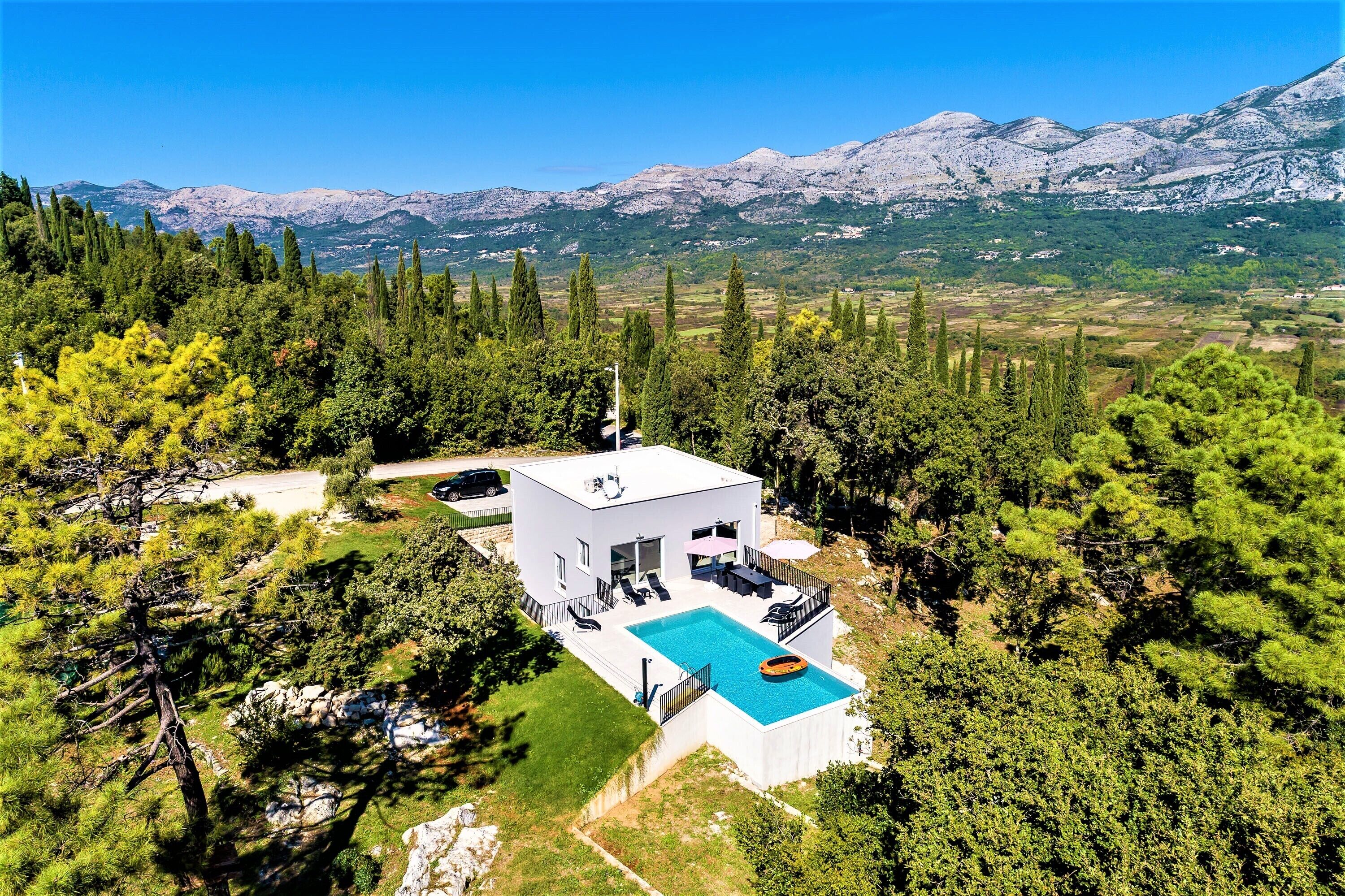 Une maison moderne à deux étages, dotée d’une piscine, entourée d’arbres et avec des montagnes en toile de fond.