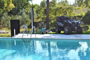 A swimming pool with a diving board, a covered seating area, and an ATV parked nearby.