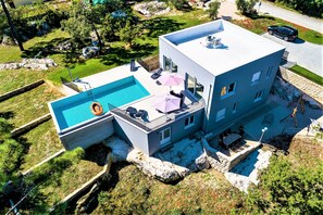 A modern two-story house with a swimming pool, outdoor seating, and a view of the surrounding landscape.