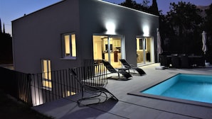 Une maison moderne dotée d’une piscine, d’un espace extérieur aménagé et d’une entrée bien éclairée.