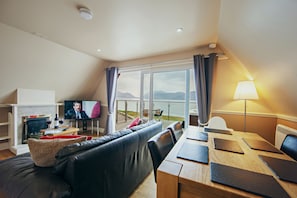 A modern living room with a sofa, a dining table, and a TV. - Waterfront Lodge 5 with Hot Tub (Kentallen Pier)