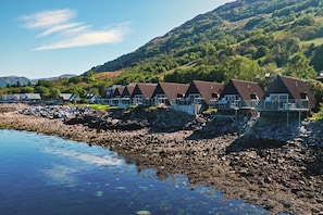Eine Reihe von Chalets mit steilen Dächern, gelegen an einer felsigen Küstenlinie, mit Hügeln und blauem Himmel im Hintergrund.