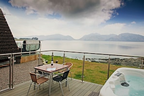 A deck with a table and chairs overlooking a body of water and mountains. - Waterfront Lodge 5 with Hot Tub (Kentallen Pier)