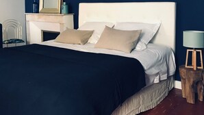 Ein Schlafzimmer mit einem weißen Bett, einem Nachttisch, einem Spiegel, einer Wandlampe und einem kleinen Holzschemel mit Lampe.