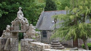 An ancient stone structure with a circular tower, surrounded by stone walls and a building with a tiled roof.