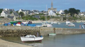 A coastal town with boats docked at a stone pier, a church with a spire, and houses along the hillside.