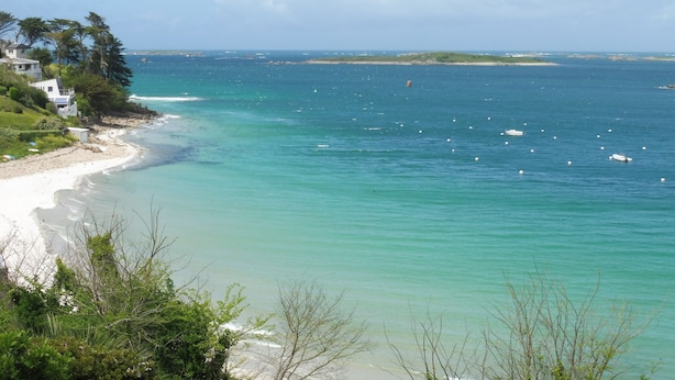 A coastal view with a sandy beach, clear turquoise waters, and a few boats.