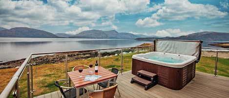 Een terras met een jacuzzi, tafel en stoelen met uitzicht op een meer en bergen in de verte.