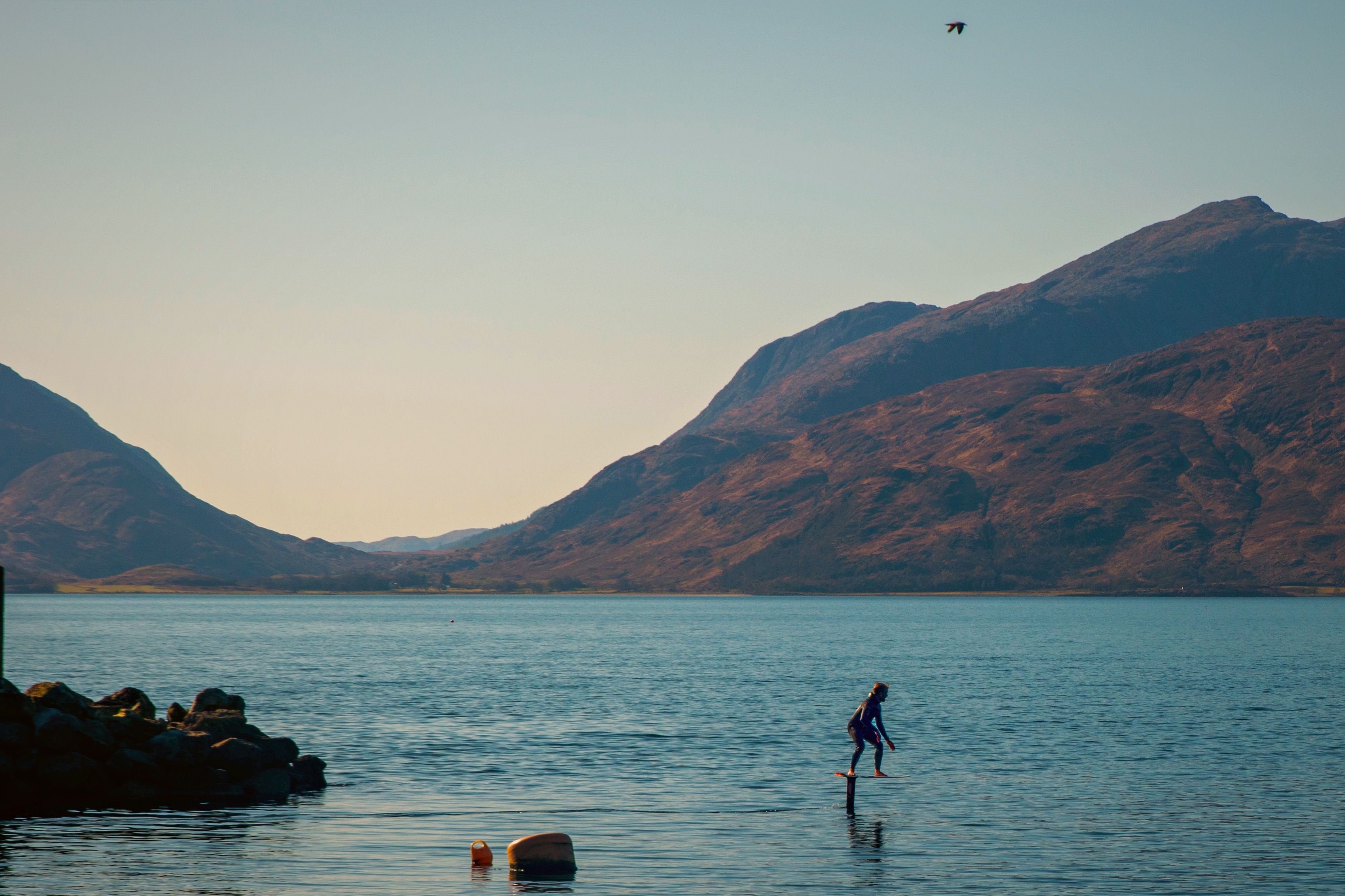 A person surfing on calm water with mountains in the background.