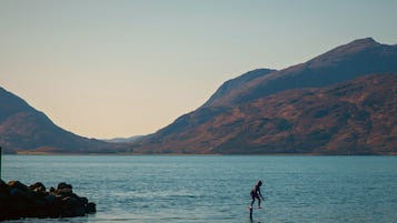 A person surfing on calm water with mountains in the background.