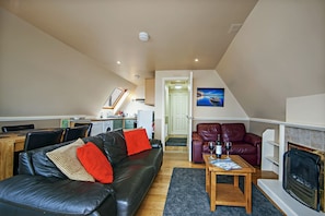 A living room with a black leather sofa, a wooden coffee table, a fireplace, and a dining area with a table and chairs. - Waterfront Lodge 4 with Hot Tub (Kentallen Pier)