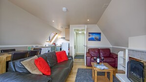 A modern living room with a black leather sofa, red cushions, a wooden coffee table, and a fireplace. - Waterfront Lodge 4 with Hot Tub (Kentallen Pier)