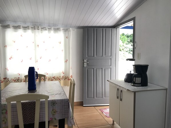 A small kitchen with a table and chairs, a coffee maker, and a door leading outside.