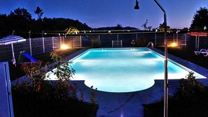 Una piscina de borde curvo, rodeada por una cerca y luces colgantes.