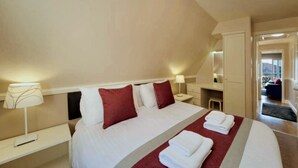 Habitación de hotel con una cama grande, dos mesitas de noche, un escritorio y una silla. Se ve una ventana con vistas al exterior.