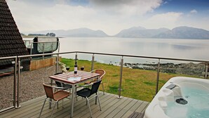 Una terraza con mesa y sillas frente a un cuerpo de agua y montañas.