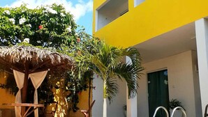 A pool area with a yellow building, a thatched-roof structure, and palm trees. - Pousada Amarante praia (São Miguel do Gostoso)