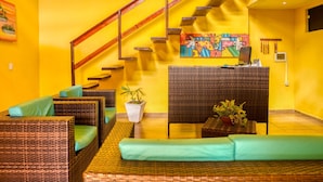 A bright yellow interior with wicker furniture, a staircase, and a colorful painting. - Pousada Amarante praia (São Miguel do Gostoso)