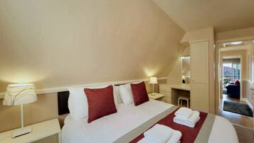 A hotel room with a large bed, two bedside tables, a nightstand, a desk, and a chair. There is a window with a view of the outside.