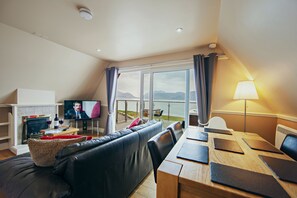 A modern living room with a sofa, a TV, a fireplace, and a dining area with a table and chairs. - Waterfront Lodge 8 with Hot Tub (Kentallen Pier)