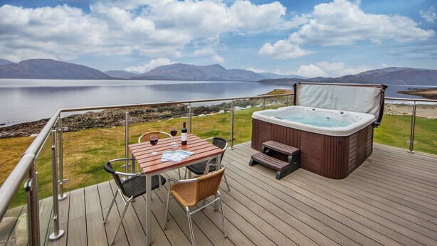 Een terras met een jacuzzi, tafel en stoelen met uitzicht op een meer en bergen op de achtergrond.